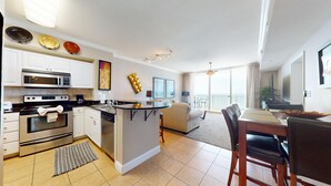 A modern kitchen with built-in appliances, a dining area with a table and chairs, and a balcony with a view. - Tidewater 509 -Gulf front - Amazing views! (Panama City Beach)