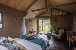 A bedroom with a large bed, a chair, a small table, and a balcony with a view. - Sleep Whiskers Away From the Lions and " Feel " Them Roar! Cabin 4 (The Crags)