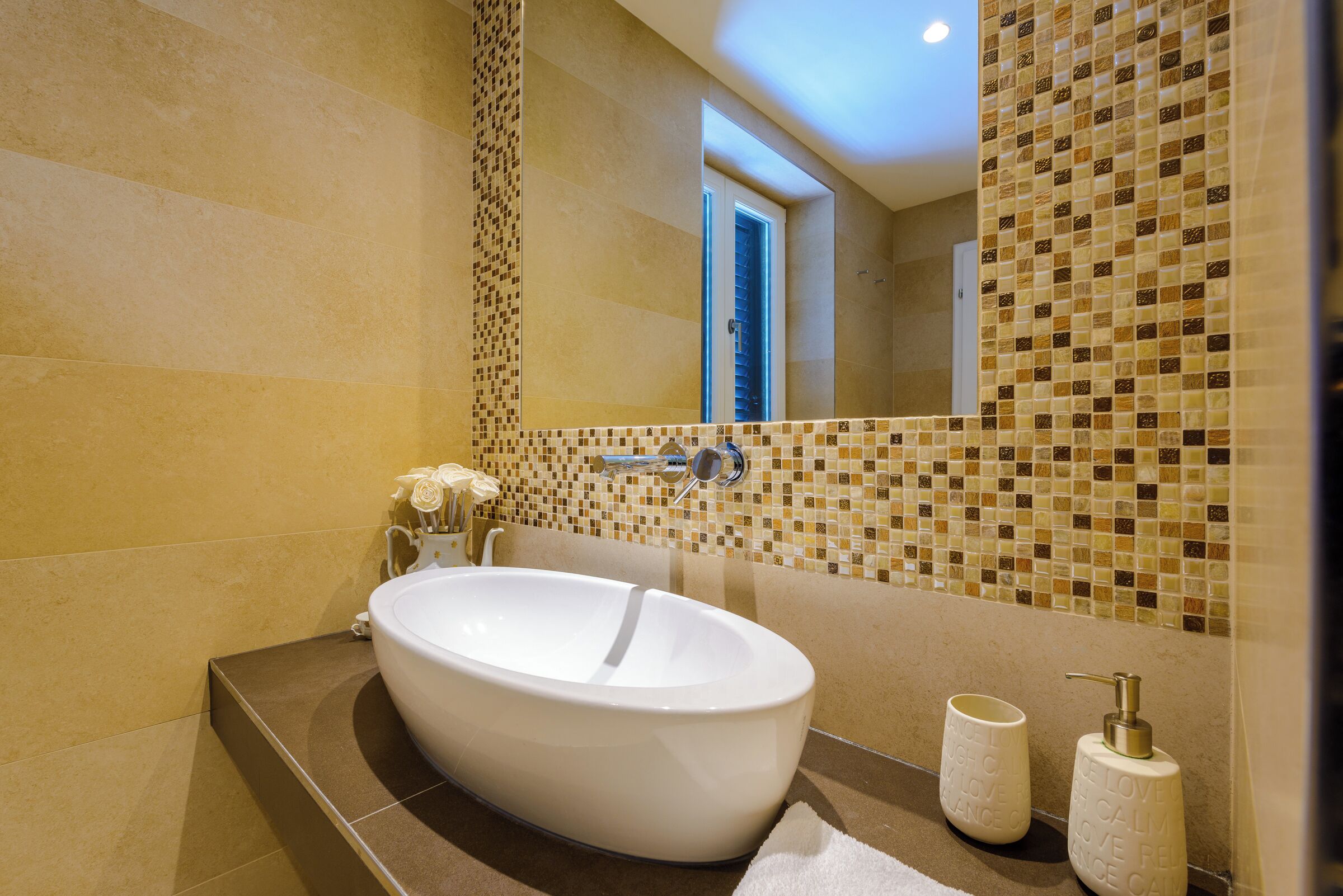 A modern bathroom with a large oval sink, a mirror, and a mosaic tile backsplash.