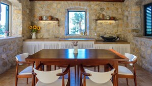 A stone-walled dining area with a wooden table and white chairs, a window with a view of trees, and shelves with decorative items. - Villa Family and friends, Dubravka (Dubravka)