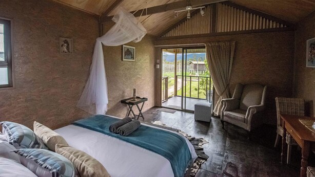 A bedroom with a large bed, a chair, a small table, and a balcony with a view. - Sleep Whiskers Away From the Lions and " Feel " Them Roar! Cabin 3 (The Crags)
