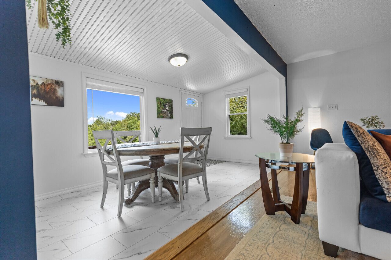 A dining area with a wooden table and chairs, a small side table, and a sofa with cushions.