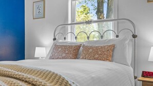 A neatly made bed with floral pillows, a metal headboard, and a bedside table with a clock.