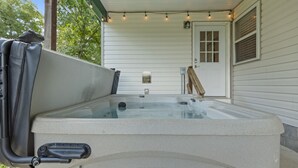 A hot tub with a pump and a step, set against a white house exterior with a door and window.