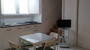 Kompakti keittiö, jossa on valkoiset kaapit, kaasuliesi ja pieni ruokailutila, jossa on pöytä ja tuolit.