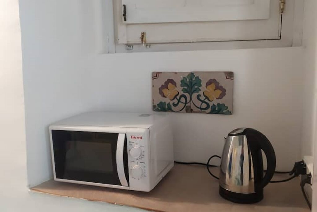 Un four à micro-ondes blanc est posé sur une étagère en bois, une bouilloire se trouve à droite, et une mosaïque décorative est fixée au-dessus du four à micro-ondes.