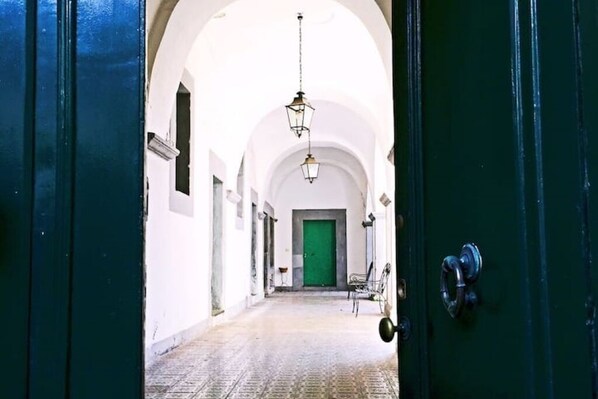 A corridor with a green door, white walls, and a hanging light fixture.
