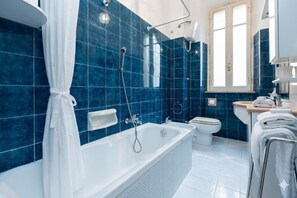 Une salle de bain équipée d’une baignoire, de toilettes et d’un lavabo, avec des carreaux bleus et un rideau blanc.