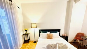 Une chambre d’hôtel avec un lit bien fait, une table de chevet avec une lampe, une chaise et une petite table sur laquelle est posé un vase de fleurs.