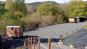 Un espace de stationnement recouvert de gravier, avec un abri en bois et un petit bâtiment doté d’un toit en pente.