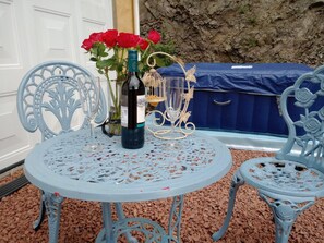 A round table with a decorative metal top, surrounded by two ornate blue chairs. A bottle of wine and a glass are on the table, with a vase of red roses in the background. - Llandovery - Cottage - Sleeps4 - Parking Secure Lock up for Bikes (Llanwrtyd Wells)