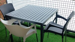 A table and two chairs set on artificial grass, with a wire mesh fence in the background. - Rustenburg Cozy Apartment With Private Entrance & BBQ (Rustenburg)