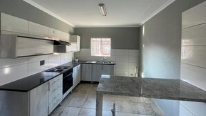 A modern kitchen with grey cabinets, a black countertop, and a window with blinds. - Rustenburg Cozy Apartment With Private Entrance & BBQ (Rustenburg)