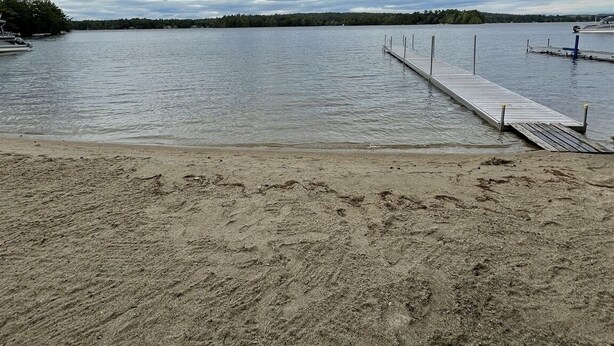 A sandy beach with a wooden dock extending into calm water.