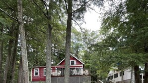 A cabin surrounded by tall trees, a wooden deck, and a staircase leading up to the house.
