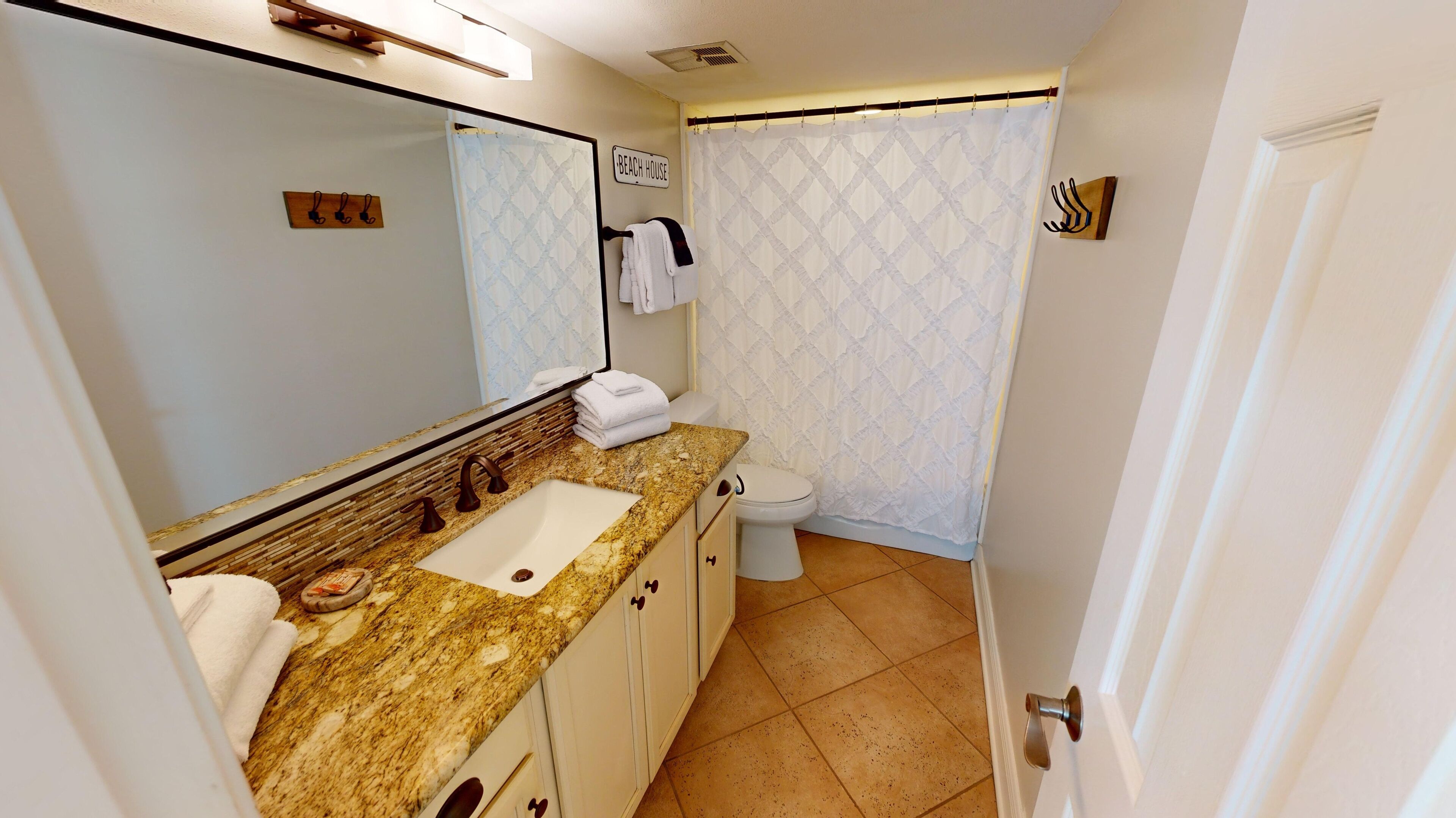 A bathroom with a granite countertop sink, a mirror, a toilet, and a shower curtain.