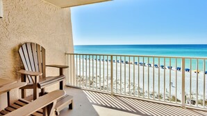A balcony with a view of a beach, a wooden chair, and a table. - Beach House 301a 2 Bedroom Condo (Miramar Beach)
