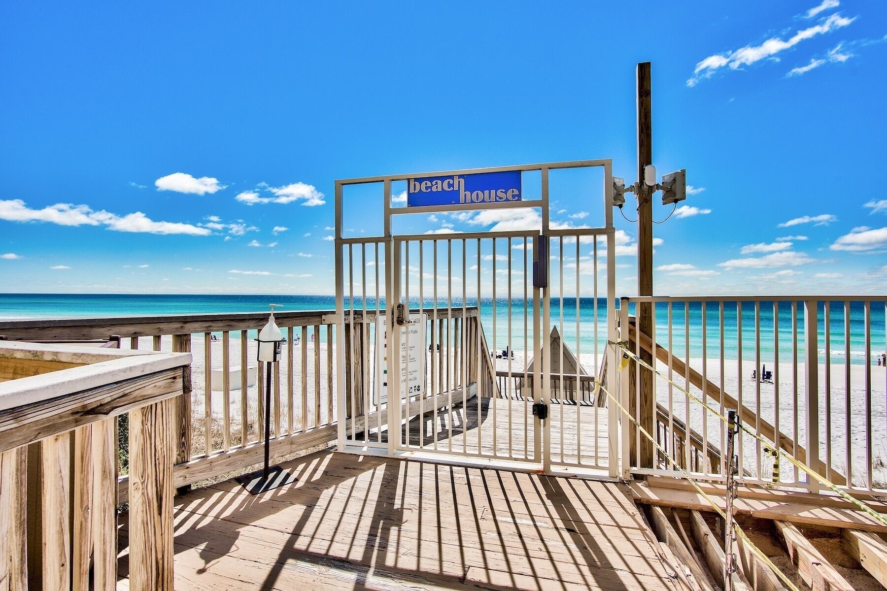 A wooden deck leading to a beach house with a clear view of the ocean.
