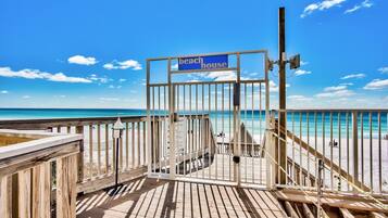 A wooden deck leading to a beach house with a clear view of the ocean.