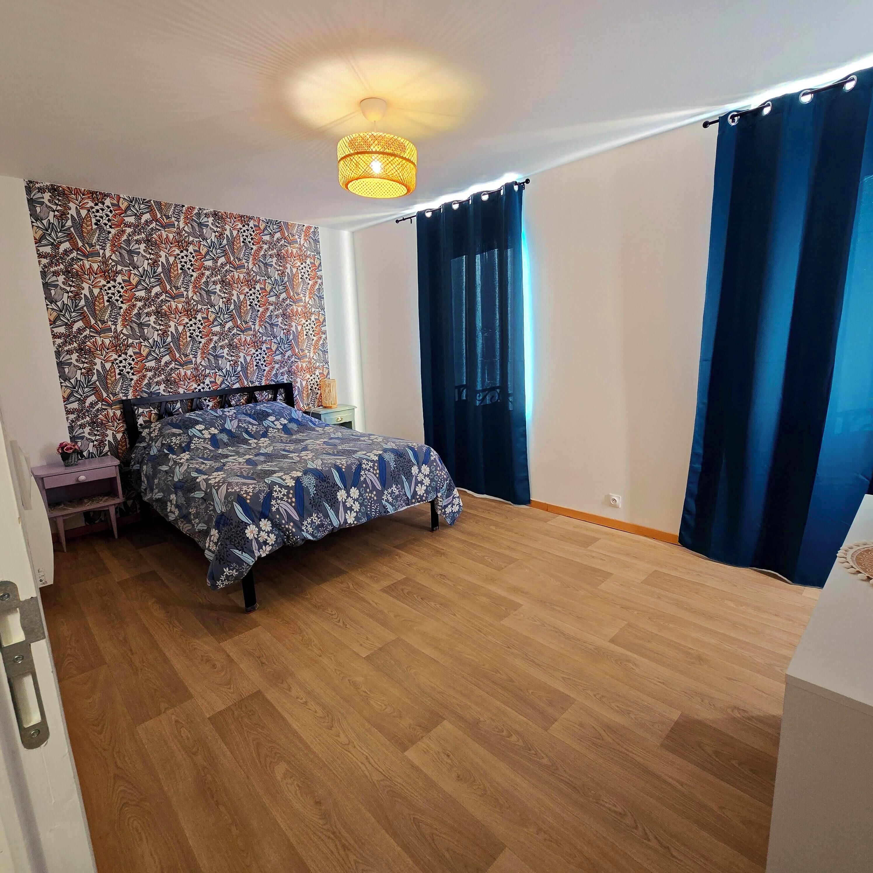 A bedroom with a bed, a nightstand, a patterned wall, and a ceiling fan.