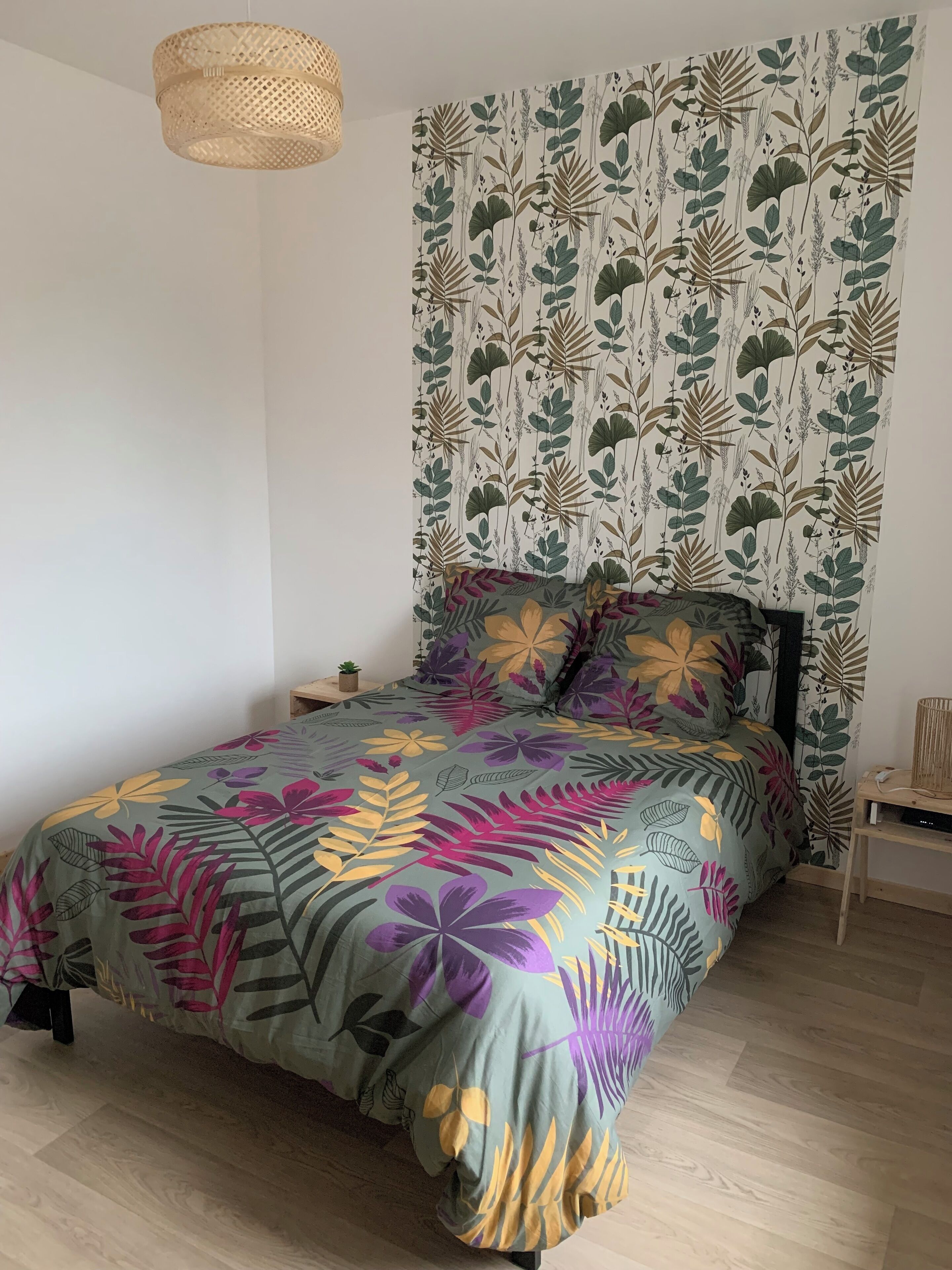 Et soveværelse med en seng, et natbord, en lampe og en væg med bladmotiv.