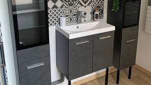 A modern bathroom with a grey cabinet, a white sink, and a mirror above it. There are decorative tiles on the wall behind the sink. - RENOVATED HOUSE SLEEPS 6 - SPACIOUS LIVING ROOM - WI-FI - FREE PARKING (Arthun)
