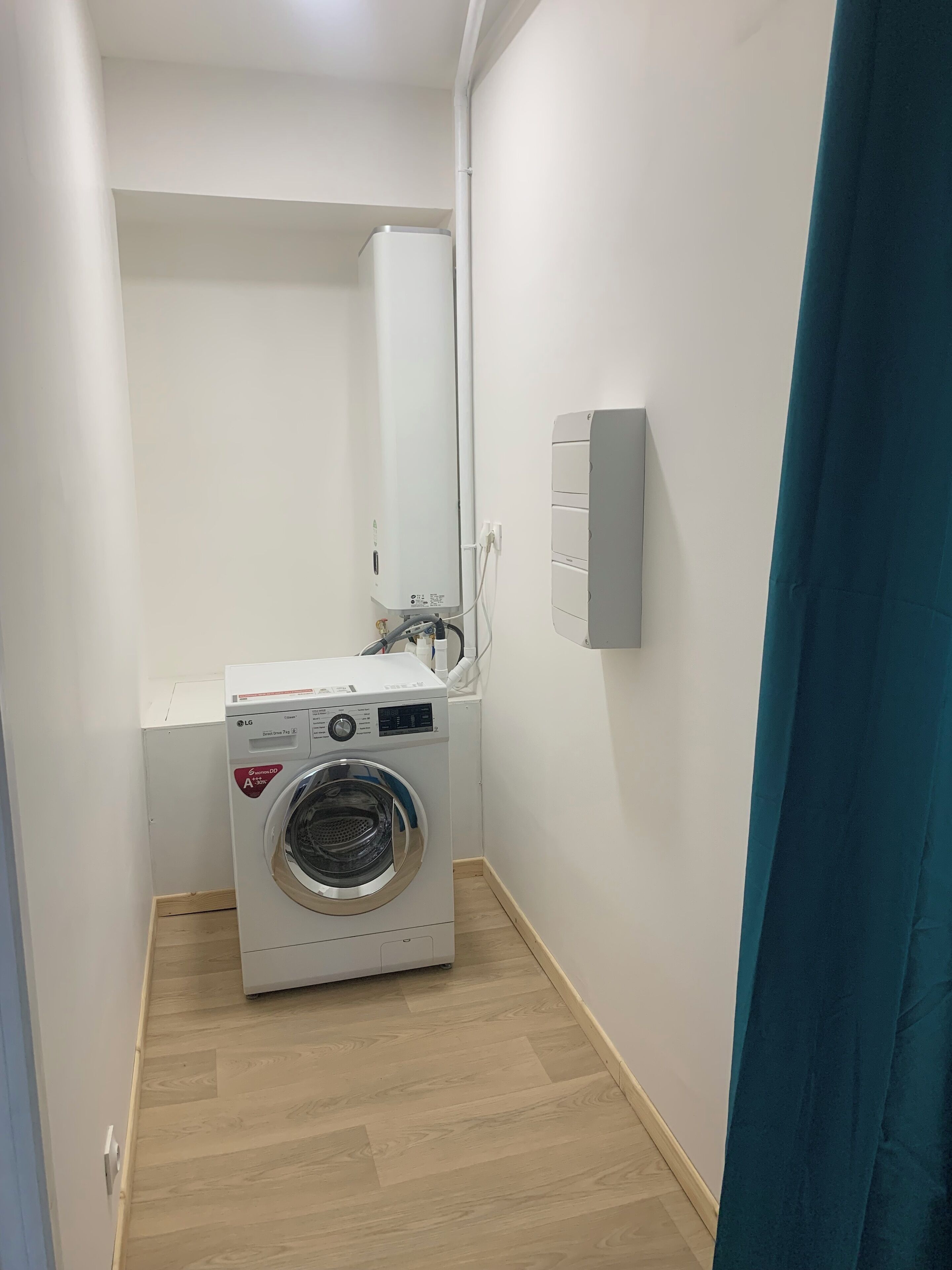 Een kleine wasruimte met een voorlader wasmachine, een klein wastafeltje en een wandradiator.