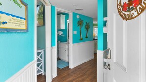 A hallway with teal walls, a white door, and a sign that reads "Beach House." - Seascape 1313 2 Bedroom Condo (Galveston)