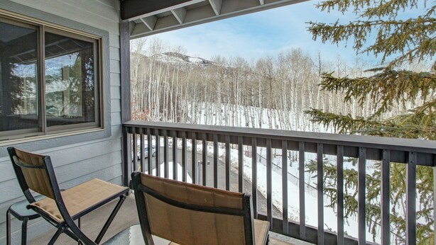 Ein Balkon mit zwei Stühlen und einem Tisch, mit Blick auf eine verschneite Landschaft mit Bäumen und blauem Himmel.