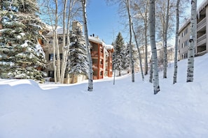 A snow-covered street with a building featuring a balcony and a wooden facade.