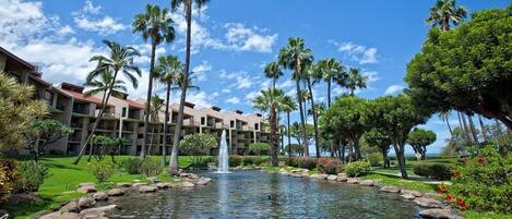 A hotel with a central water feature, palm trees, and a well-maintained garden.