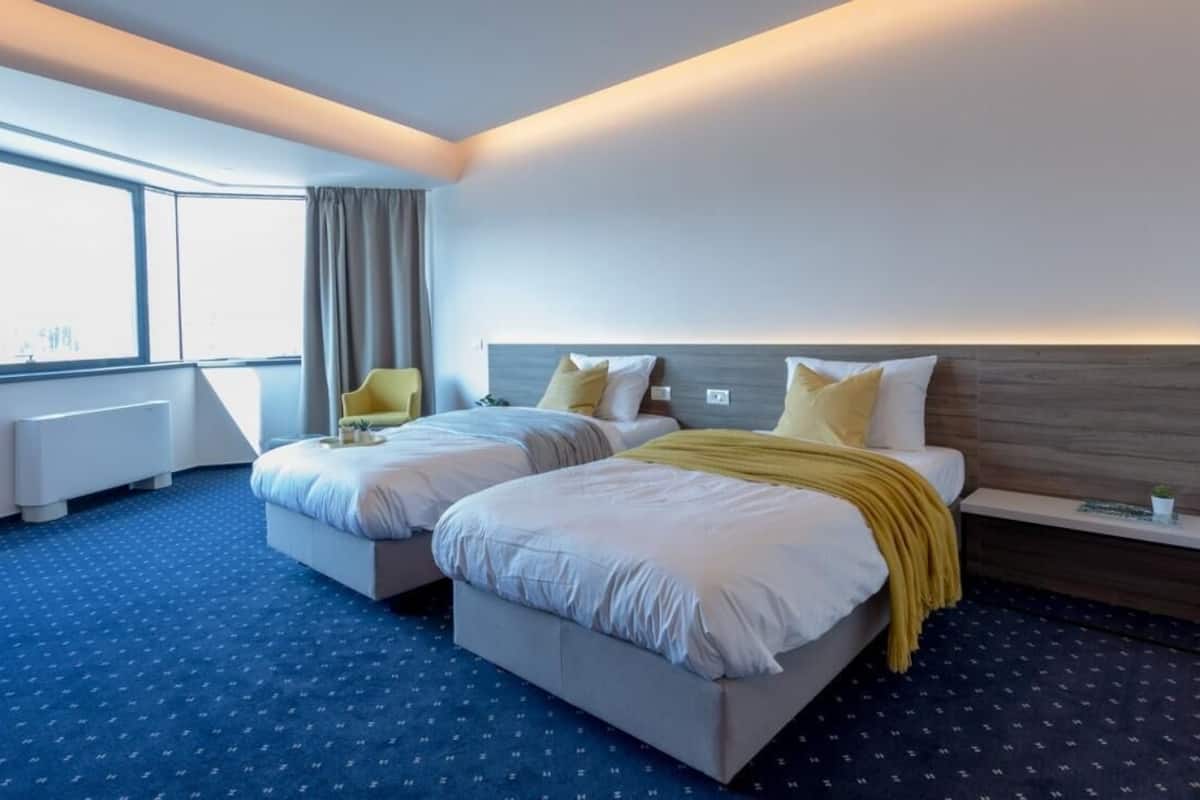 A hotel room with two beds, a large window, a view of the city, and a modern design.