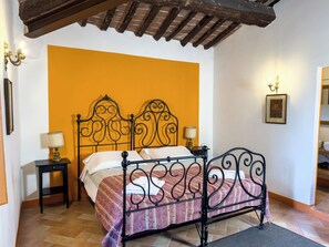 A bed with a wrought iron headboard, a bedside table with a lamp, and a large orange wall.