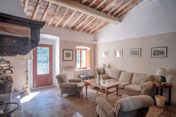 A cozy living room with a wooden ceiling, a sofa, armchairs, a coffee table, and a fireplace.