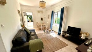 Una sala de estar con un sofá negro, una mesa de centro, un mueble para televisión y un comedor con sillas y una mesa.