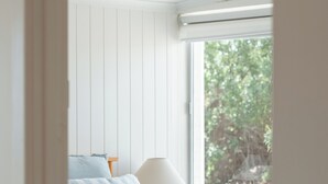 Une chambre à coucher avec un lit, une table de chevet, une lampe et une fenêtre donnant sur des arbres.