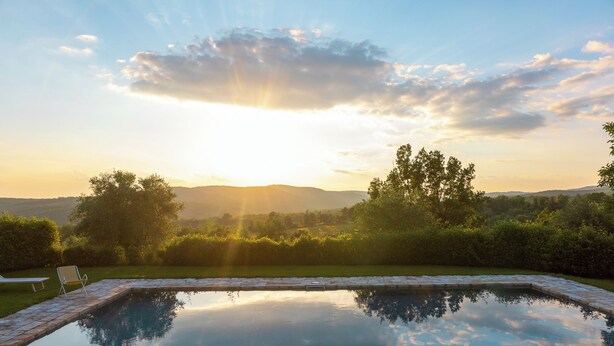 A rectangular swimming pool with stone edges, surrounded by a well-maintained lawn and trees, with a sunset in the background. - Walnut House (Toscana)