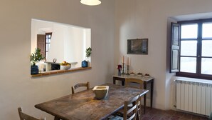 A dining area with a wooden table, chairs, a hanging light fixture, a window, and a radiator. - Walnut House (Toscana)