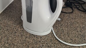 Un batedor i una olla elèctrica blanca damunt d'un taulell de granat amb un rebedor de rajola blanca.