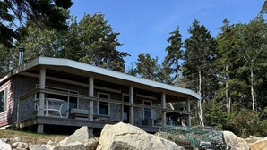 A lodge with a covered deck, large rocks in front, and a forested backdrop.