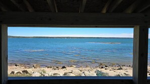 A view from a wooden structure overlooking a rocky shoreline with clear blue water and distant land.