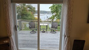 Une terrasse en bois avec deux fauteuils en osier et une petite table, donnant sur une étendue d’eau et des arbres.