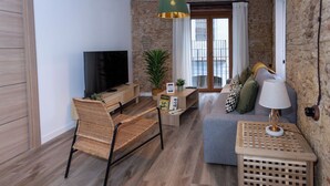 A modern living room with a flat-screen TV, wicker chairs, a grey sofa, a small wooden table, and a potted plant. - Tenerias Apart Corp S.L (Valencia)