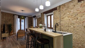 A modern kitchen with a central island, bar stools, and a stone wall. - Tenerias Apart Corp S.L (Valencia)