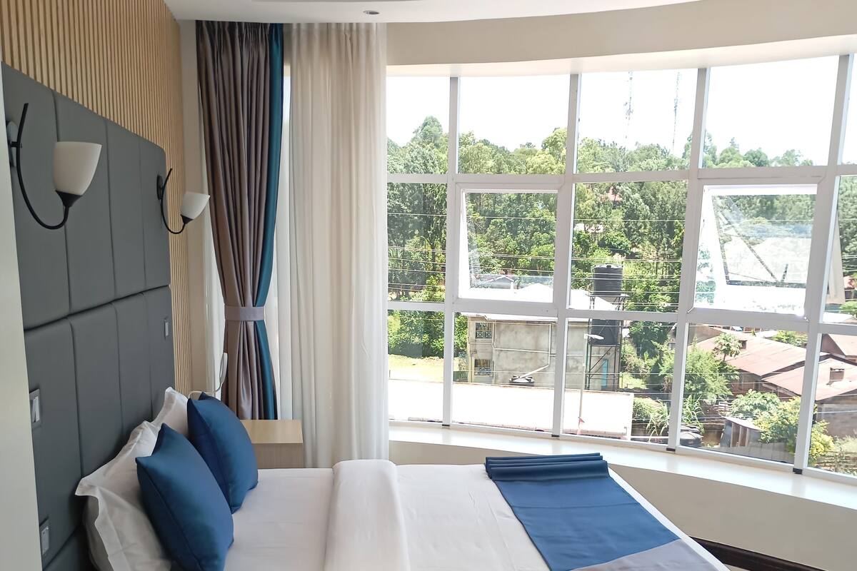 A modern hotel room with a large bed, a bedside table, and a view of the surrounding area.