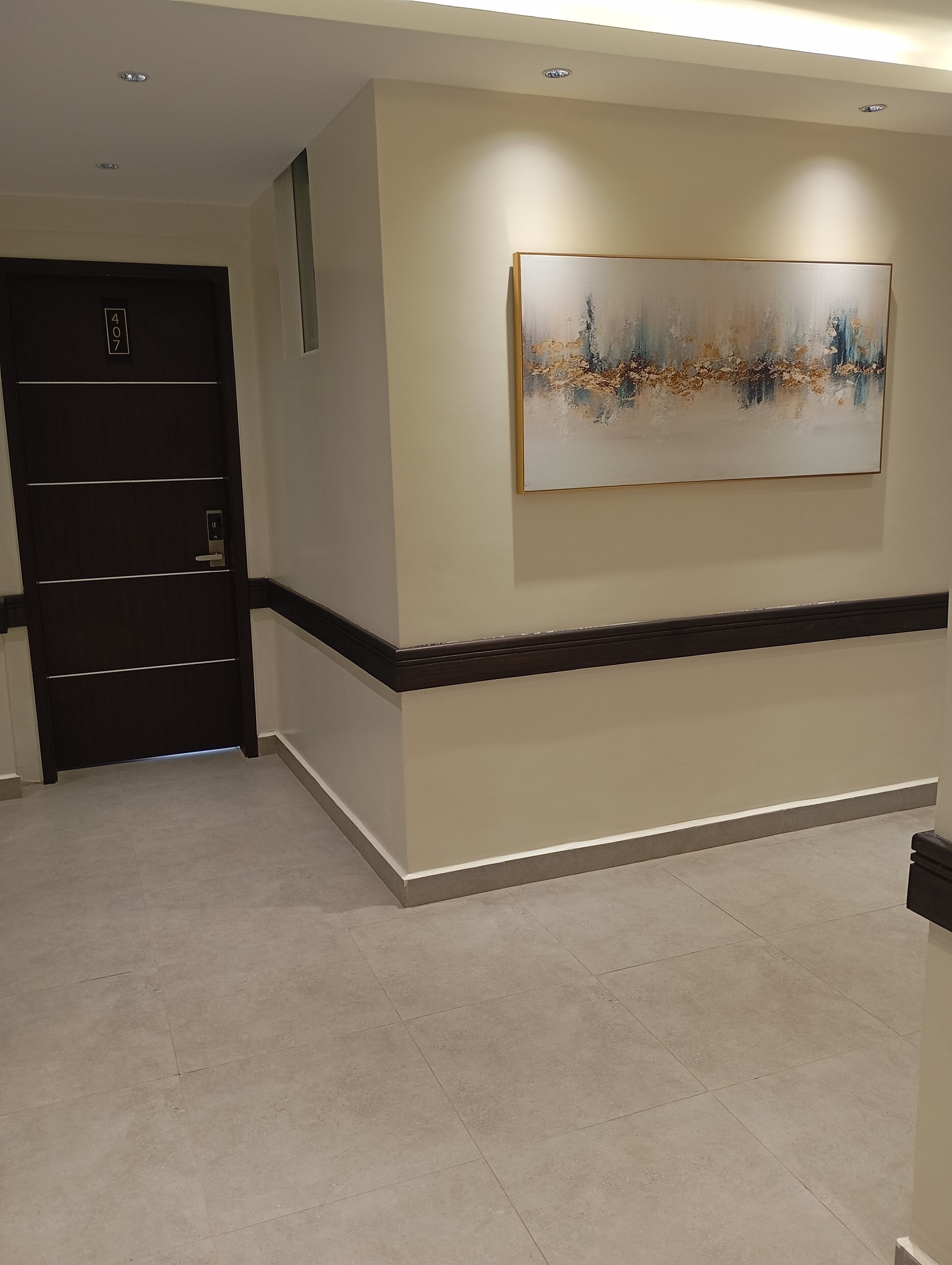 A hallway with a dark door marked '407', a beige wall, and a large abstract painting.