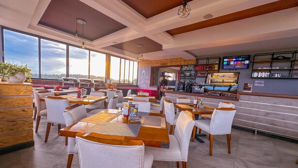 A modern restaurant with high ceilings, large windows, and a bar area. Tables and chairs are arranged for dining. - Zuri Place Hotel Limited (Oyugis)