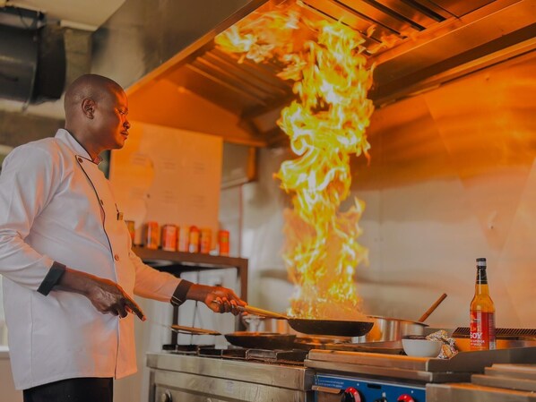 A chef cooking with flames in a kitchen. - Zuri Place Hotel Limited (Oyugis)