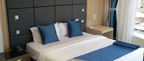 A modern hotel room with a large bed, wooden panel wall, and a view of the outside.