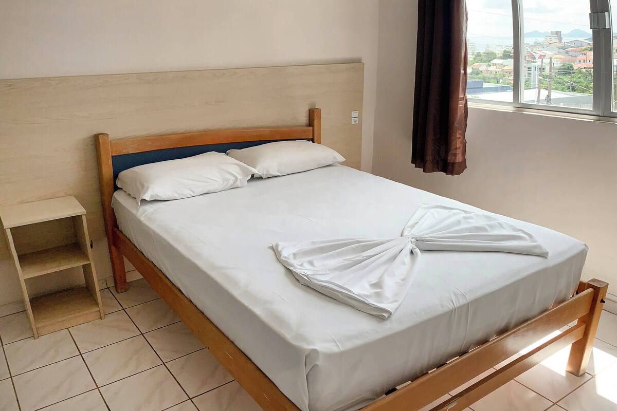 A neatly made bed with a wooden headboard, a small bedside table, and a window with curtains.